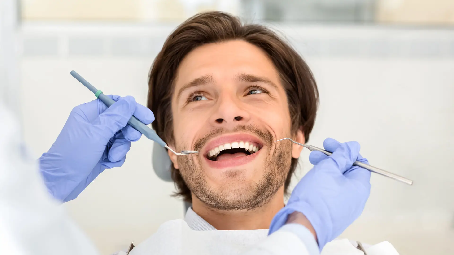 Portrait of handsome cheerful man attending dentist, looking at doctor with smile on his face